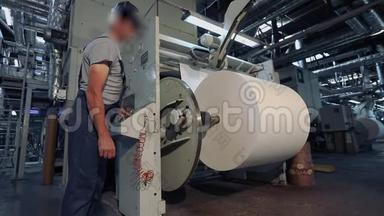 一个人站在工厂里生产壁纸。 工厂里一个人控制着机器